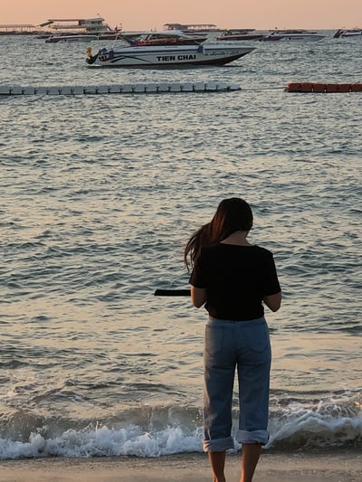 白天，一名身穿黑色衬衫和灰色粗斜纹棉布牛仔裤的妇女站在海边